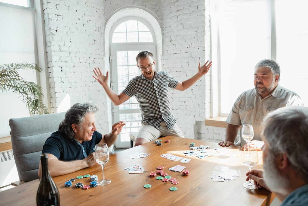 Group of happy mature friends playing cards and drinking wine