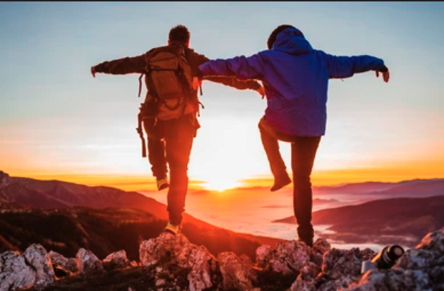 Two friends playfully balancing on a mountain ridge during sunset, symbolizing the joy of adventure, companionship, and shared experiences with a hiking buddy.