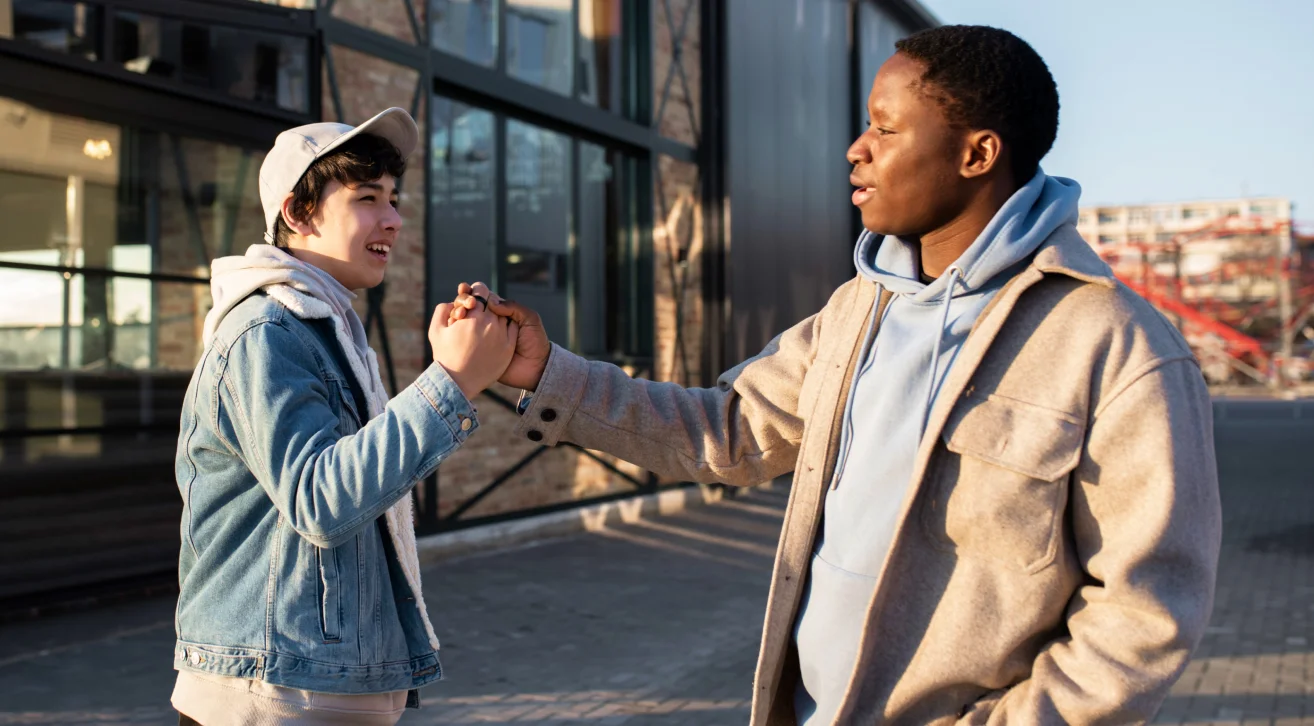 Two friends confidently greeting each other with a handshake outdoors, symbolizing overcoming social anxiety through meaningful connections and highlighting how Bunchups can provide a supportive environment for building friendships.