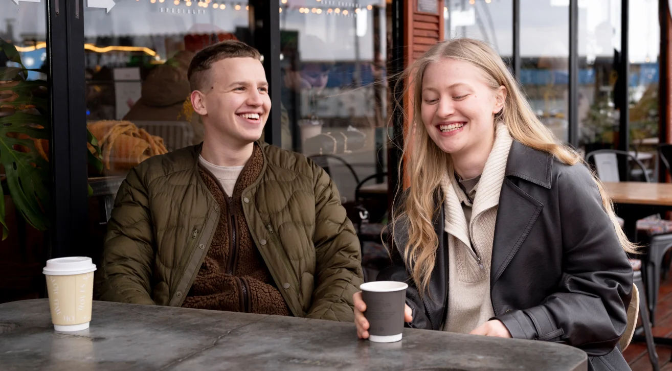 Two friends laughing and enjoying coffee together at a cozy café, representing casual and effective conversation starters , with a mention of Bunchups for meaningful small-group gatherings.